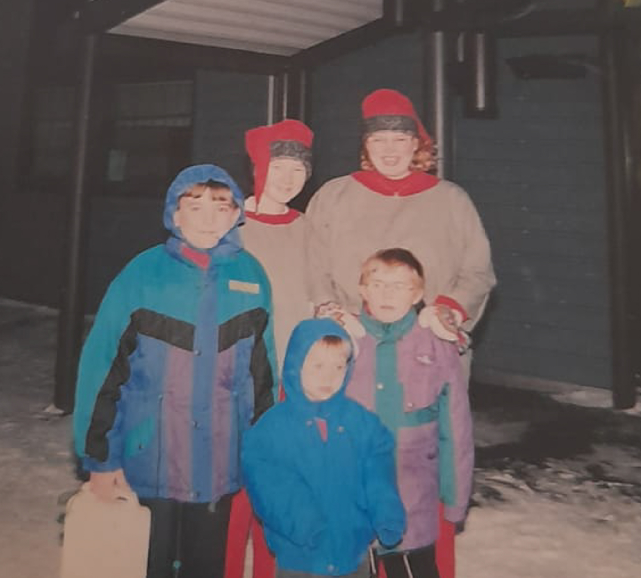 Image shows 3 children in winter clothing stood with to people dressed as elves, there is snow on the ground